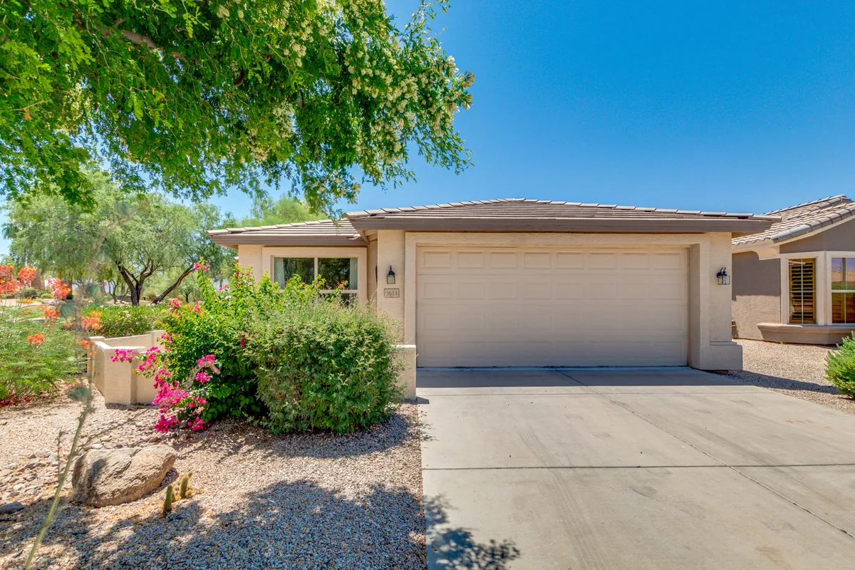 This image presents the home's front exterior featuring a welcoming garage door, well-maintained landscaping, and large windows. The scene is bright and inviting, suggestive of sunny Arizona afternoons and the home's curb appeal.