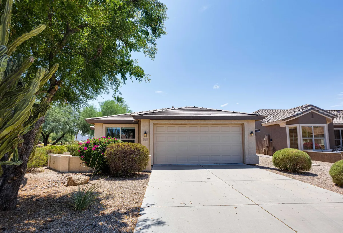 A welcoming exterior view of the home shows the front entrance, a neat garage door, and a landscaped garden. The space is bathed in natural light, with a path leading to the covered patio, suggesting a peaceful environment perfect for morning coffee or evening relaxation. The mature greenery and open neighborhood feel reflect a tranquil, safe 55+ community.