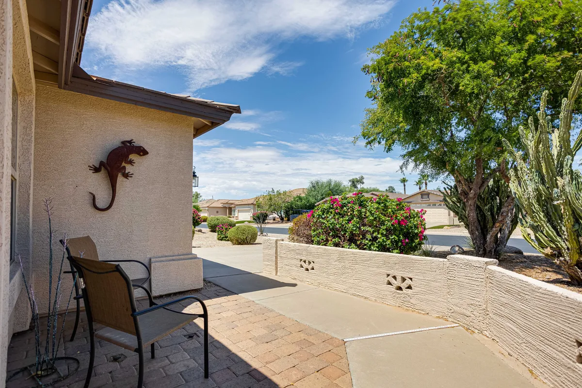 A charming scene capturing a comfortable chair on a porch surrounded by vibrant flower bushes and a decorative lizard sculpture. The space appears inviting for relaxation and socializing while enjoying views, potentially of the golf course or sunsets.
