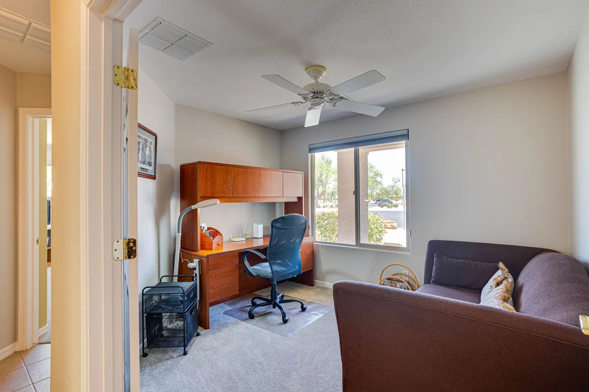 A multi-functional room with a desk, chair, large window, and a sofa creates a flexible, cozy environment suitable for working, reading, or accommodating guests. The setting appears adaptable and comfortable, reflecting the den described.