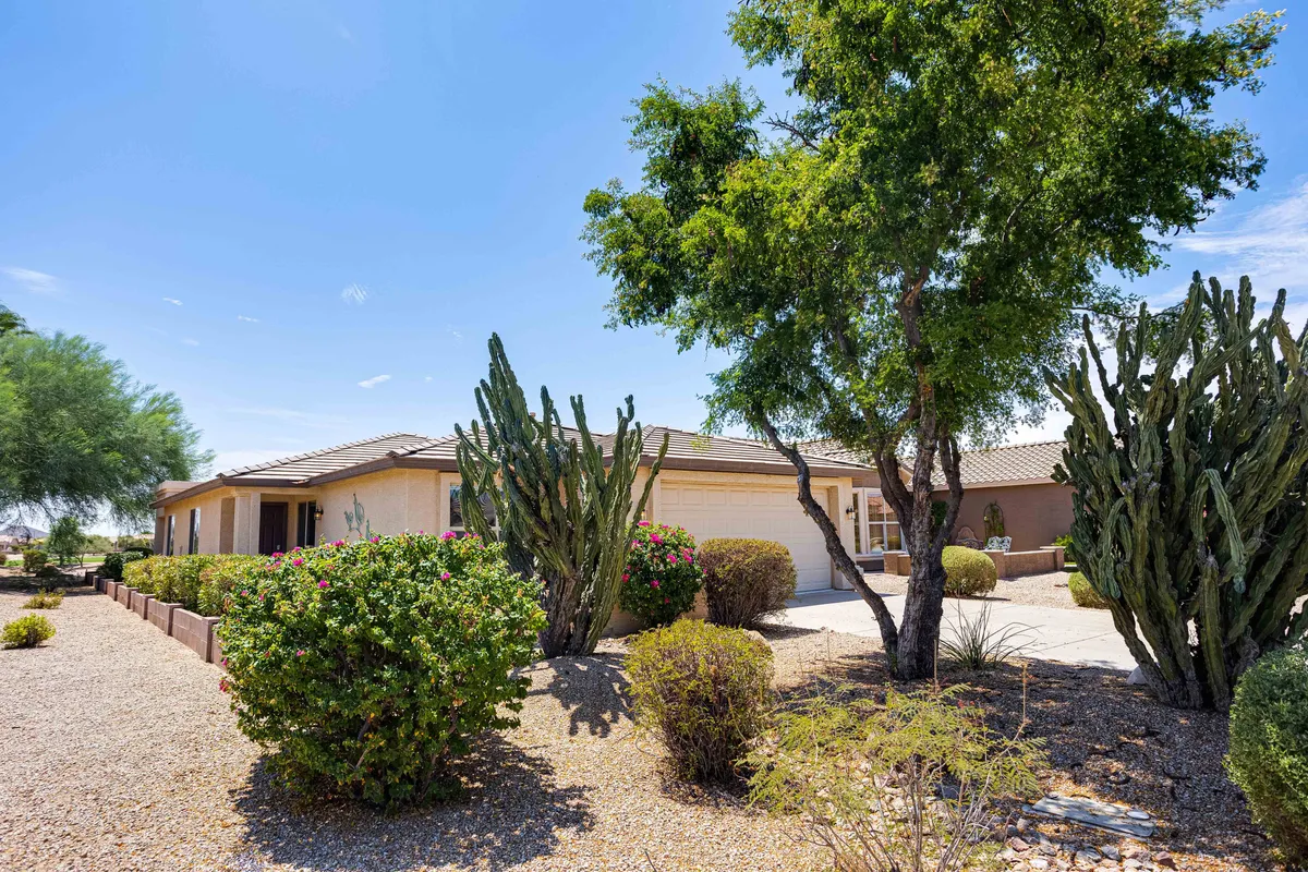 An inviting exterior shot featuring cacti, lush bushes, and the house exterior bordered by a welcoming pathway. The landscaping hints at the proximity to open spaces and the outdoors, ideal for stepping out to the golf course.