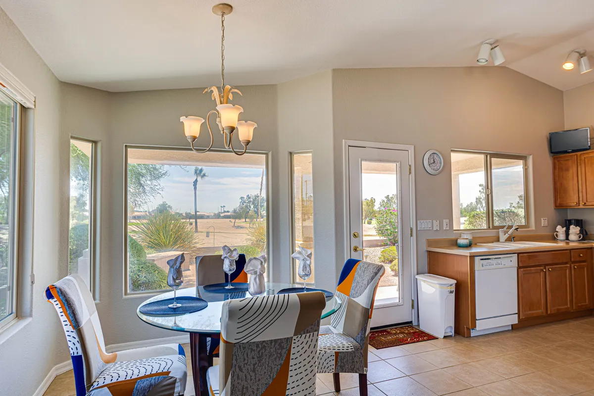 A cheerful dining area with a round table surrounded by colorful chairs, set beside expansive windows that let in morning sun. The inviting setup hints at the transition from kitchen to dining, with plenty of space for family meals or gatherings.