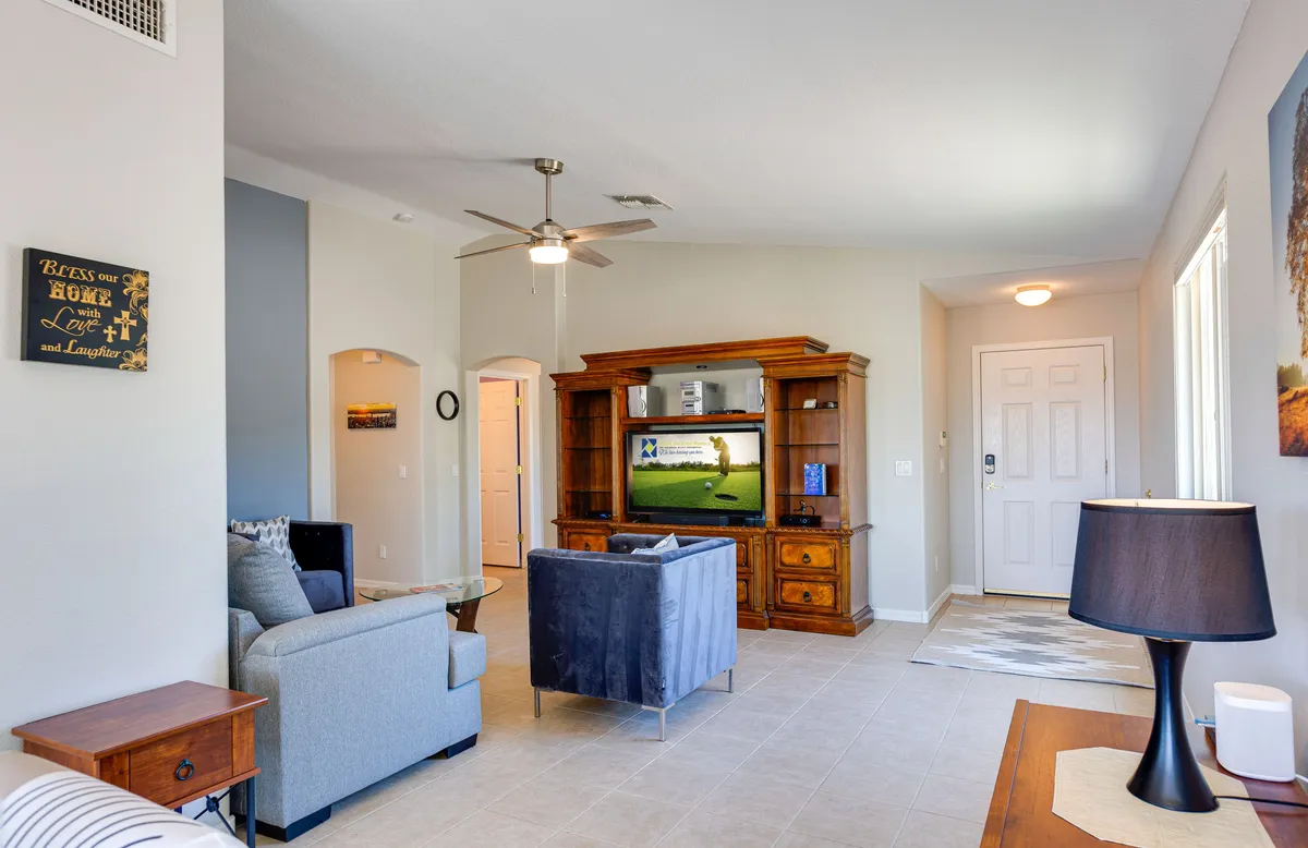 A spacious, sunlit living area featuring a comfortable sofa, elegant wooden entertainment center with television, and views toward the front door. The warm, casual setting invites relaxation, family gatherings, and quiet moments, aligning with the home’s focus on comfort and quality time.