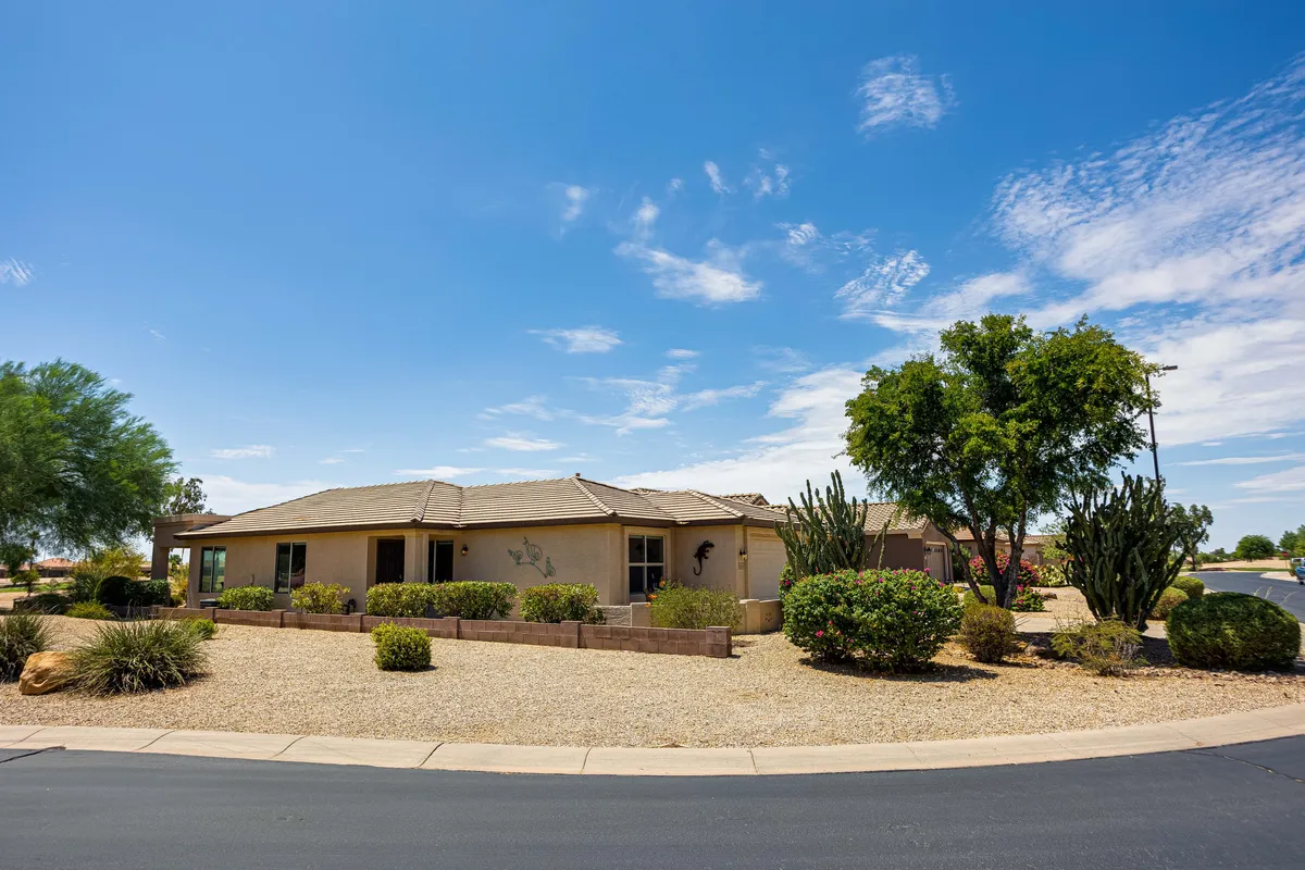A broad exterior shot of the home set amid cacti, trees, and well-maintained landscaping, with ample space for gatherings and activities. The scene hints at group events and outdoor recreation in a vibrant desert setting.