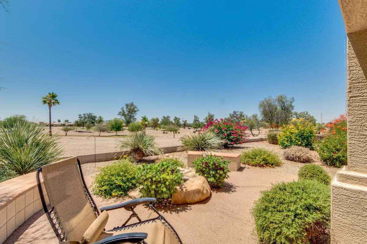 This tranquil backyard scene highlights comfortable patio chairs, vibrant flowers, and distant palm trees. The arrangement encourages relaxation and socializing while offering views of the surrounding landscape and a sense of privacy and calm.