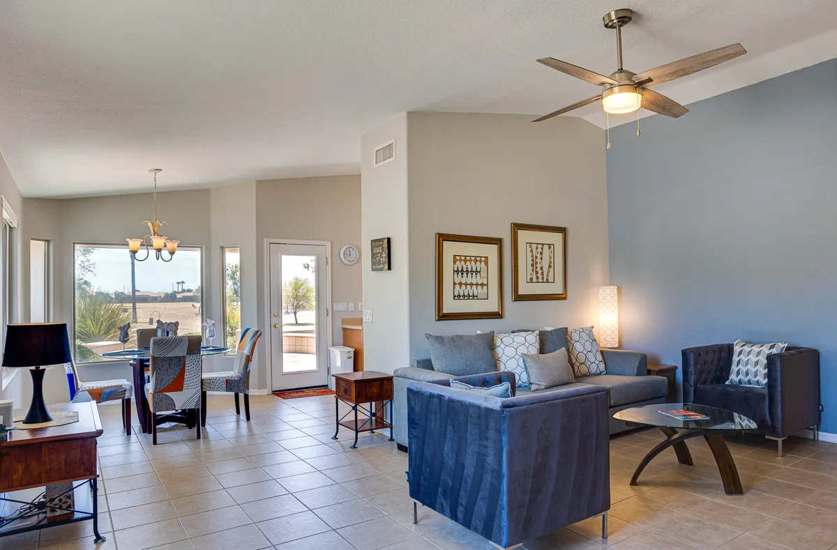 A welcoming, open-plan living area with a sofa, dining table, decorative artwork, and a ceiling fan. The space is arranged for both relaxation and small-group socializing, with a cozy, inviting ambience.