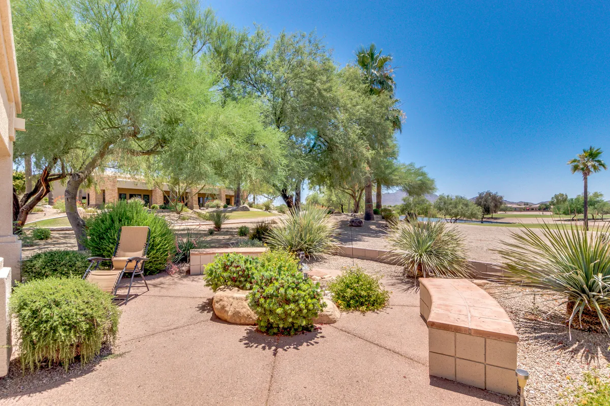 This image features a serene backyard scene with lush greenery, a stone bench, a comfortable lounge chair, and a beautiful desert landscape beyond. The space is designed for relaxing outdoors and enjoying nature, with inviting spots for reading or leisurely gatherings.