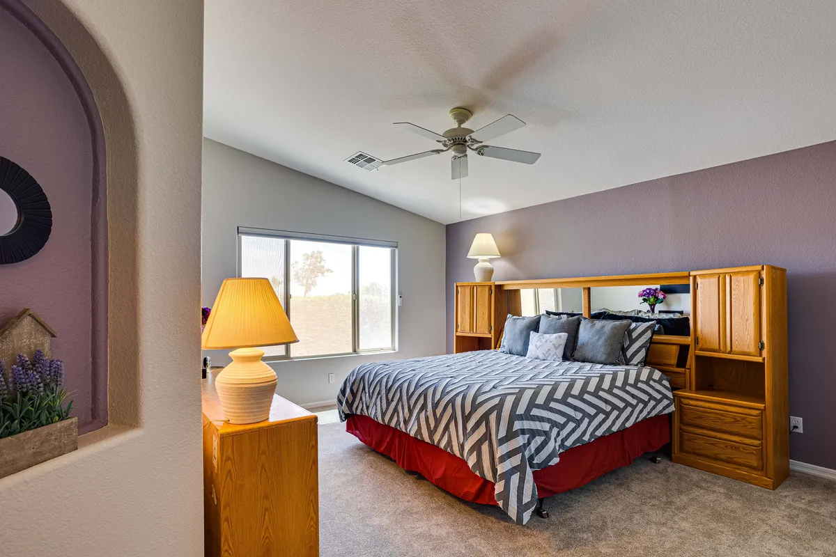 A cozy bedroom displaying a queen bed dressed in chevron-patterned bedding, a large window letting in soft sunlight, wooden furniture, and a decorative lamp. The gentle mood suggests comfort and relaxation, ideal for guests or family.